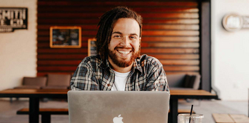A student sits at his computer and smiles